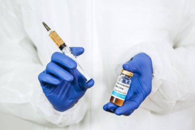 Beyaz cüppeli ve mavi eldivenli bir doktor, içinde koronavirüs aşısı olan bir şırınga tutuyor. Covid-2019 'dan aşı enjekte edildi. Pandemik koronavirüs 2020. Aşı testi.