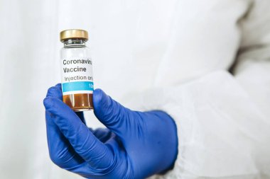 Doktor beyaz arka planda Coronavirus aşısı olan bir test tüpü tutuyor. Covid-19 aşısı. 2020 Salgını. Doktorun elleri mavi tıbbi eldivenlerde. Virüsün tedavisi..