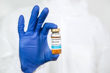 Doktor beyaz arka planda Coronavirus aşısı olan bir test tüpü tutuyor. Covid-19 aşısı. 2020 Salgını. Doktorun elleri mavi tıbbi eldivenlerde. Virüsün tedavisi..