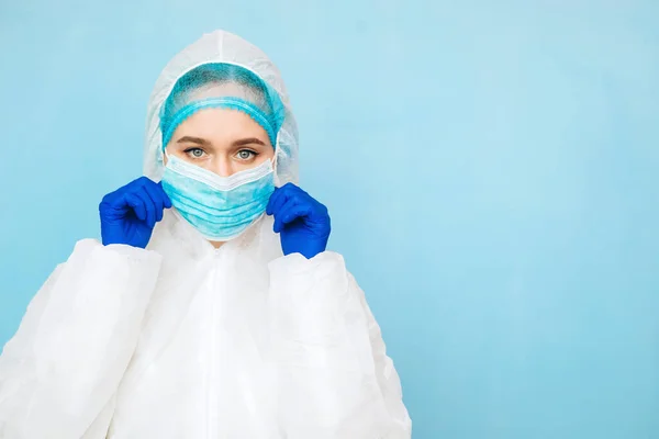 Mavi arka planda koruyucu giysili bir doktor. Kız doktor koruyucu tulum, maske ve mavi eldiven giyiyor. Salgın covid-2019. Corona virüsü. Virüs 2020. Maskeli doktorun portresi..