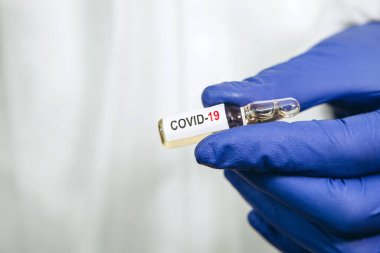 Doktor beyaz arka planda Coronavirus aşısı olan bir test tüpü tutuyor. Covid-19 aşısı. 2020 Salgını. Doktorun elleri mavi tıbbi eldivenlerde. Virüsün tedavisi..