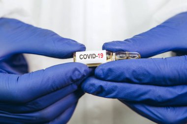 Doktor beyaz arka planda Coronavirus aşısı olan bir test tüpü tutuyor. Covid-19 aşısı. 2020 Salgını. Doktorun elleri mavi tıbbi eldivenlerde. Virüsün tedavisi..
