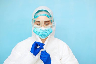 Mavi arka planda koruyucu giysili bir doktor. Kız doktor koruyucu tulum, maske ve mavi eldiven giyiyor. Salgın covid-2019. Corona virüsü. Virüs 2020. Maskeli doktorun portresi..