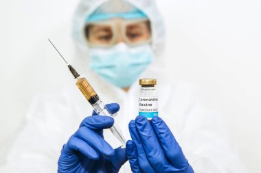 Bir tıp laboratuarı çalışanı bir şişe aşı ve şırınga taşıyor. Doktorun elleri çok yakın. Covid-2019. 2020 Salgını. Virüse karşı aşı. Beyaz cüppeli ve mavi eldivenli doktor..