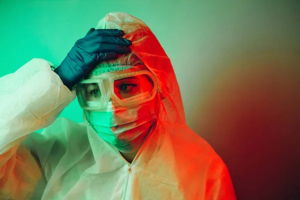 Siyah arka planda koruyucu giysili genç kız doktor. Kasvetli ışıklandırma. Yorgun doktor. Salgın covid-2019. Gözlüklü, eldivenli ve maskeli bir doktorun portresi. Koronavirüsün yayılmasını engelle.