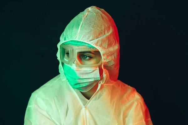 young girl doctor in protective clothing on a black background. Gloomy lighting. Tired doctor. Epidemic covid-2019. Portrait of a doctor in glasses, gloves and a mask. stop the spread of coronavirus.