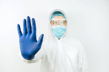 Tıbbi maskeli doktor, tulumlu ve beyaz arka planda mavi eldivenli. Covid 2019 salgınını durdurun. Doktor dur işaretini elleriyle gösteriyor..