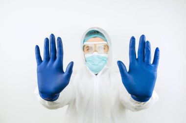 Tıbbi maskeli doktor, tulumlu ve beyaz arka planda mavi eldivenli. Covid 2019 salgınını durdurun. Doktor dur işaretini elleriyle gösteriyor..