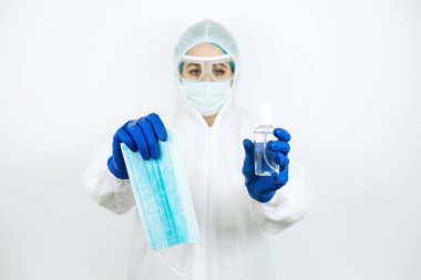 Elinde dezenfektanla beyaz arka planda duran tıbbi maskeli bir doktor. Coronavirüs salgınında dezenfektan kullanımı. COVID 2019. Doktorlara yardım et - evde kal.