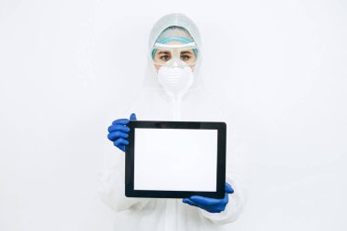 Koruyucu giysili doktor, solunum cihazı, gözlük, eldiven bir tablet / telefon tutuyor. Mesaj için yer. Doktorlar koronavirüs salgını sırasında evde kalmalarını tavsiye ettiler. COVID-19