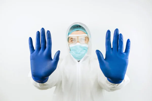 Tıbbi maskeli doktor, tulumlu ve beyaz arka planda mavi eldivenli. Covid 2019 salgınını durdurun. Doktor dur işaretini elleriyle gösteriyor..
