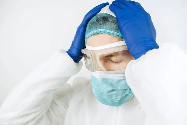 close-up portrait of tired doctor after shift in the hospital. The doctor in protective clothing - glasses, mask, gloves on white background. The doctor treating patients with coronavirus. Covid-2019