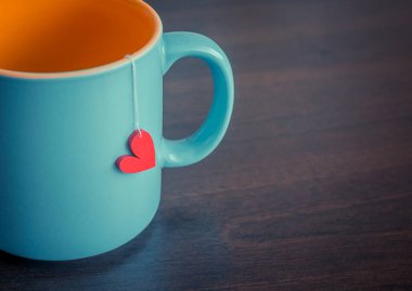 Koyu ahşap masada kırmızı kalp şeklinde çay poşeti ahşap süslemeli, seçici odaklı.