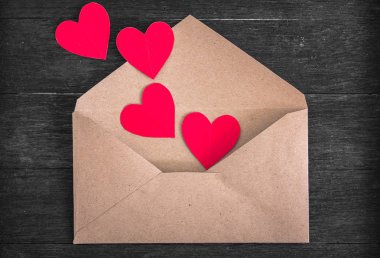 Ahşap zemin üzerinde kırmızı kağıt kalpler olan kahverengi zarf