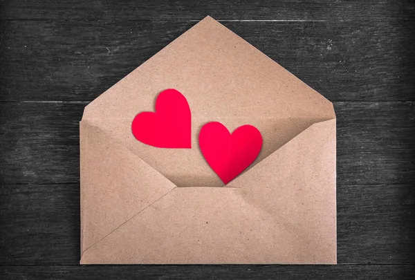 Ahşap zemin üzerinde kırmızı kağıt kalpler olan kahverengi zarf