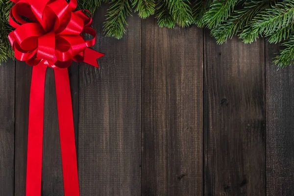 Karanlık rustik woode üzerinde kırmızı kurdele ile Noel köknar ağacı dalları