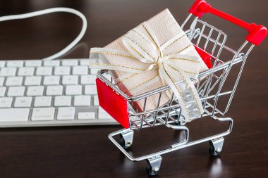 Koyu kahverengi masada alışveriş arabası ve klavyeli hediye kutusu.