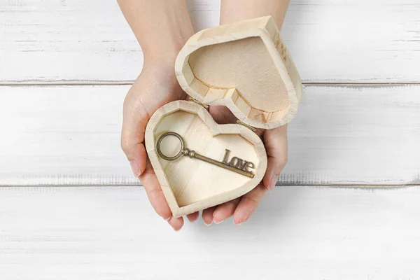 Mulher mãos segurar antigo amor chave dentro caixa do coração em madeira branca — Fotografia de Stock
