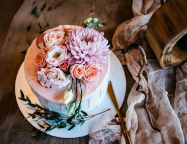 Masa ve kumaş arka planında taze çiçekler ve otlarla süslenmiş beyaz bir tabakta güzel bir beyaz pasta.