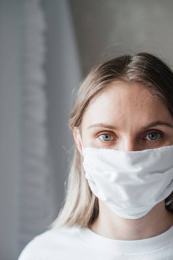 Maskeli, kısa saçlı, beyaz tişörtlü genç bir kız, evde, yakın plan. Coronavirus. Karantina