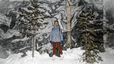 Gri şapkalı ve güzel bir kış manzarasının arka planında beyaz çizmeleri olan mavi ceketli bir kız. Karelya 'da kış