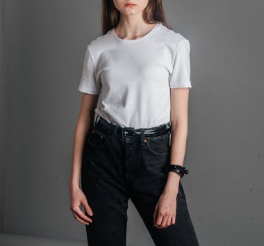 Poz veriyor. Siyah kotla poz veren yüksek bel, kemer ve beyaz tişört giyen bir manken. Poz verme dersleri. Stüdyoda fotoğraf çekimi. Kadın pozu