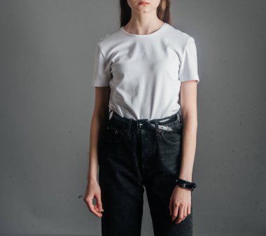 Poz veriyor. Siyah kotla poz veren yüksek bel, kemer ve beyaz tişört giyen bir manken. Poz verme dersleri. Stüdyoda fotoğraf çekimi. Kadın pozu