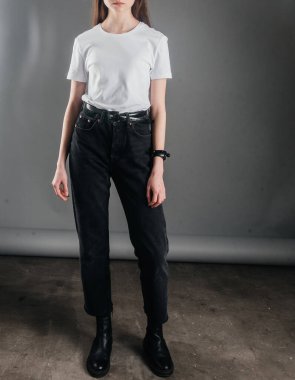 Poz veriyor. Siyah kotla poz veren yüksek bel, kemer ve beyaz tişört giyen bir manken. Poz verme dersleri. Stüdyoda fotoğraf çekimi. Kadın pozu