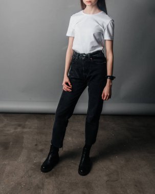 Poz veriyor. Siyah kotla poz veren yüksek bel, kemer ve beyaz tişört giyen bir manken. Poz verme dersleri. Stüdyoda fotoğraf çekimi. Kadın pozu