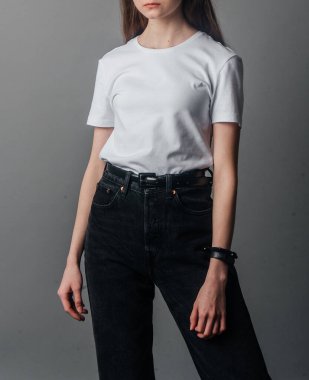 Poz veriyor. Siyah kotla poz veren yüksek bel, kemer ve beyaz tişört giyen bir manken. Poz verme dersleri. Stüdyoda fotoğraf çekimi. Kadın pozu