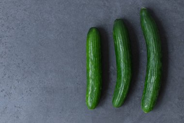 Üç taze salatalık koyu bir masada yatıyor. Farklı boyutlarda salatalıklar. Kapatın. Üst Manzara. Boş boşluk.