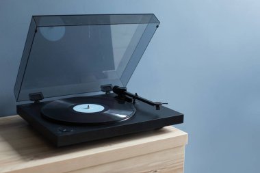 Mavi duvarın yanındaki masada vinil diski olan bir plak çalar. Boş yer
