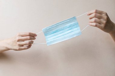 Genç bir kadın elinde tıbbi bir maske tutuyor. Kızın elinde arka planda koruyucu bir maske var. Sağlık hizmetleri kavramı