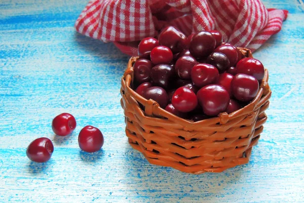 Ripe cherries in basket on old wooden table on countryside against summer foliage in sunlight — Stock Photo, Image