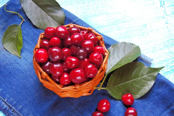 Cerezas maduras en canasta sobre una vieja mesa de madera en el campo contra el follaje veraniego a la luz del sol — Foto de Stock