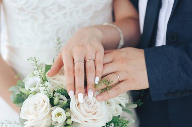 Gelin ve damadın elleri düğün buketinin arka planında.