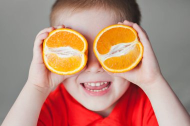 Neşeli küçük bir çocuk portakalları tutar ve gözlerine koyar. Turuncu ruh hali. Turuncu ruh hali.