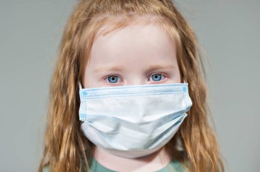 Tek kullanımlık maske takan kızıl saçlı küçük bir kız.
