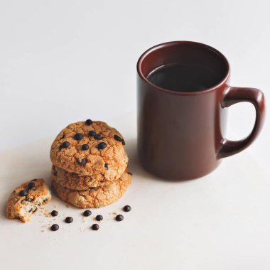 Bir fincan kahve ve beyaz arka planda çikolata parçacıklı Amerikan kurabiyesi. Yukarıdan görünüşü.