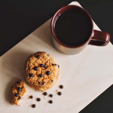 Bir fincan kahve ve beyaz arka planda çikolata parçacıklı Amerikan kurabiyesi. Yukarıdan görünüşü.