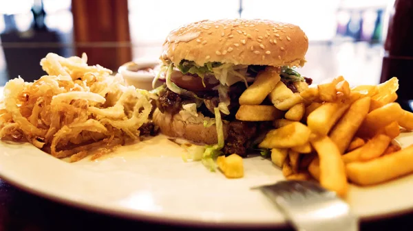 Ohälsosam måltid med mexikanska nachochips, nötkött burger, laddad med ost, pommes frites, lökringar — Stockfoto