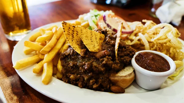 Comida poco saludable con nacho chips mexicanos cargados de carne de res, queso, papas fritas, aros de cebolla —  Fotos de Stock