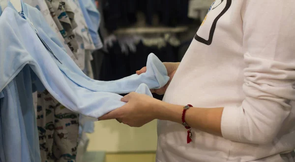 Шопінг молода жінка, ручний перегляд стоїть синій костюм для новонародженого хлопчика в магазині . — стокове фото
