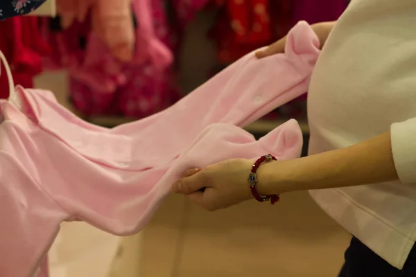 Genç kadın alışveriş, el ile görüntüleme stand dükkanda yeni doğan kız pembe elbisesi