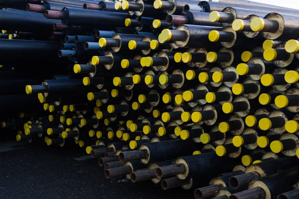 Зберігається багато чорних сталевих труб з теплоізоляцією на будівельному майданчику в обгортці пластикових труб, що лежить з жовтими кришками труб — стокове фото