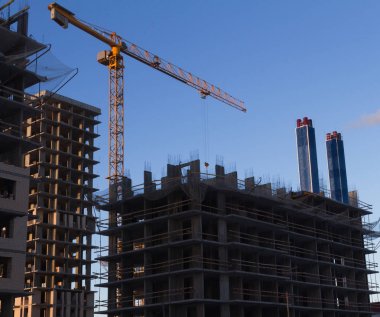 İnşaat alanında bir çok öykülü bina, sarı mavi gökyüzü arka plan üzerinde metal paneller vinç kurulumu İnşaat