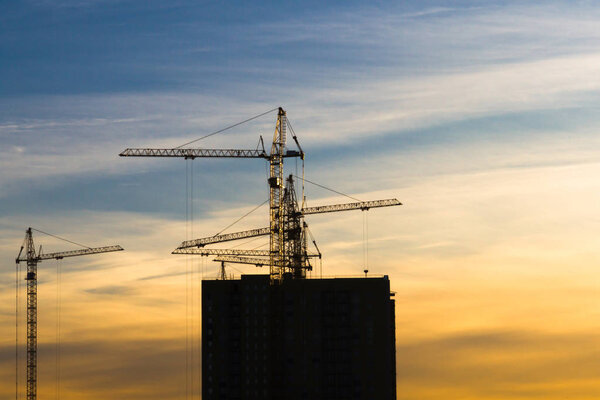 Several cranes crane yellow finish building multi-storey residential building at sunset on blue sky background