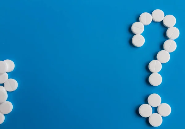 Píldoras médicas blancas signo de interrogación sobre fondo azul, imagen conceptual. Medicamentos para el tratamiento de pacientes Imagen De Stock