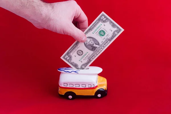 Cassetta dei soldi, sotto forma di autobus di ceramica con un taglio di due dollari, su sfondo rosso. Il concetto di risparmio di denaro. Cumulo per il riposo Foto Stock Royalty Free