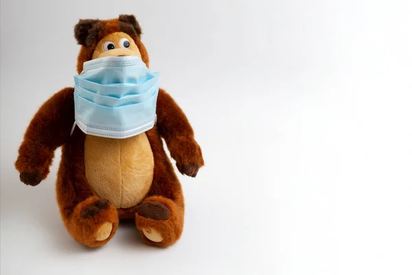 Brinquedo de crianças em uma máscara protetora com um fundo leve e uma cópia do espaço. Um urso de peluche com uma máscara médica . Fotos De Bancos De Imagens